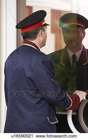 Stock Image - Hotel Doorman Reflected in Glass Door. Fotosearch
