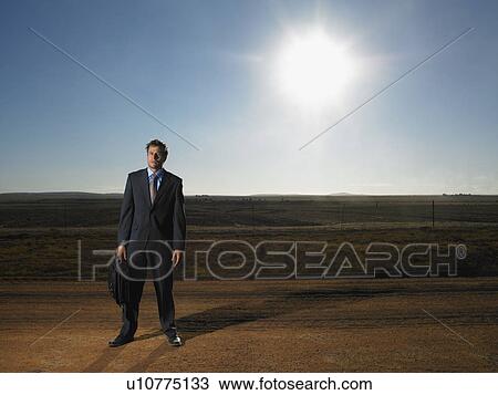 Stock Image - Isolated businessman standing in deserted road. Fotosearch