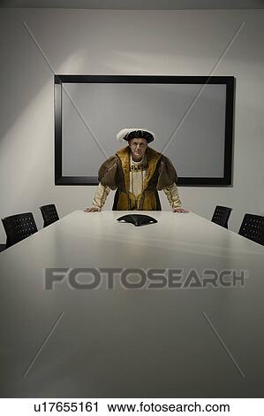 Stock Image - King Henry VIII standing at table in conference room. Fotosearch