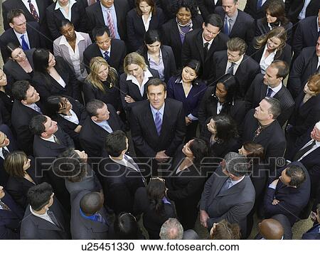 Stock Image - Large group of business people surrounding man looking up, elevated view. Fotosearch