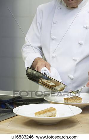 Stock Photograph - Male chef holding frying pan, serving food onto dishes in kitchen. Fotosearch