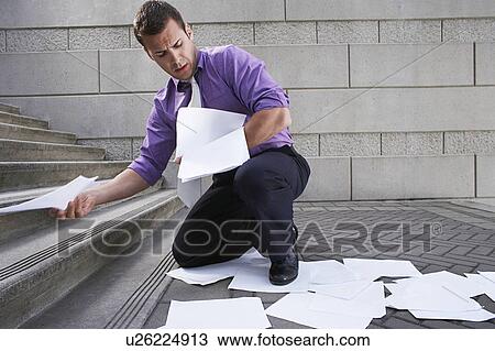 Stock Image - Man collecting spilled paperwork from steps. Fotosearch