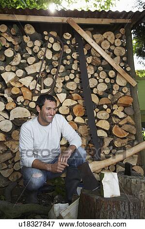 Stock Photo - Man crouching beside axe at timber shed. Fotosearch