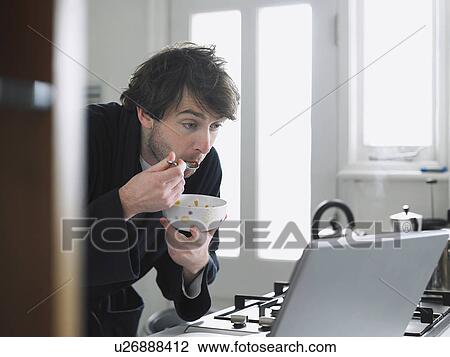 Man eating breakfast cereal while looking at laptop screen View Large Photo Image Stock Image - Man eating breakfast cereal while looking at laptop screen. Fotosearch