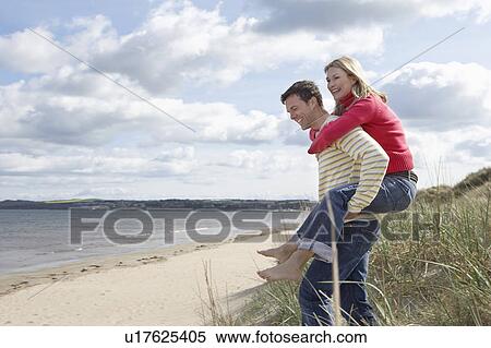 Stock Photography - Man giving woman piggy back at beach. Fotosearch