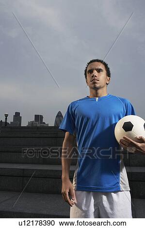 Stock Image - Man holding soccer ball, outdoors. Fotosearch