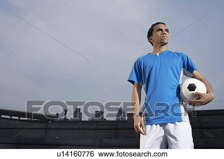 Stock Photograph - Man holding soccer ball, outdoors. Fotosearch