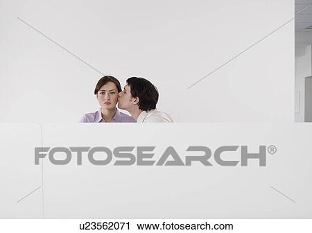Stock Image - Man kissing female colleagues cheek, in office cubicle. Fotosearch