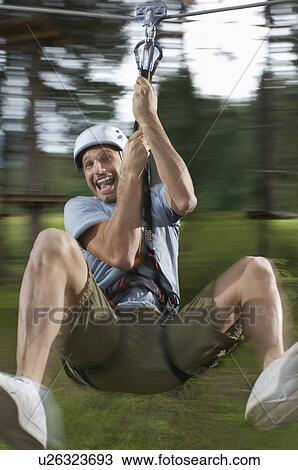 Stock Image - Man riding zip-line in forest. Fotosearch