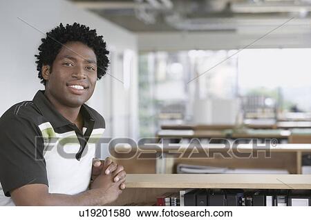 Stock Image - Man sitting in office, smiling, portrait. Fotosearch