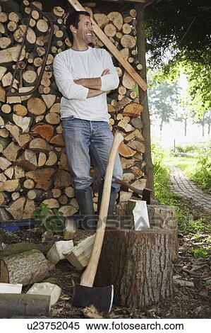 Stock Photography - Man standing by axe at timber shed. Fotosearch