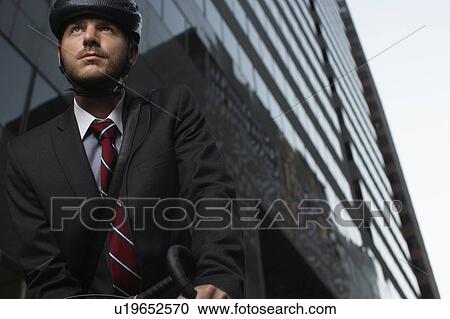 Stock Image - Man standing by bicycle in street, low angle view. Fotosearch