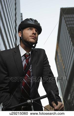Stock Image - Man standing by bicycle in street, low angle view. Fotosearch