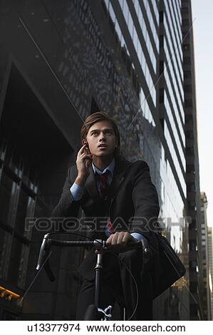 Man standing by bicycle in street, talking on mobile phone, low angle view View Large Photo Image Picture - Man standing by bicycle in street, talking on mobile phone, low angle view. Fotosearch