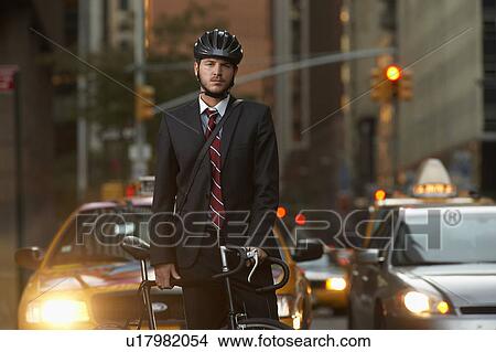 Picture - Man standing by bicycle in street, portrait. Fotosearch