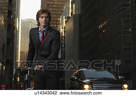 Man standing by bicycle in street View Large Photo Image Stock Image - Man standing by bicycle in street. Fotosearch