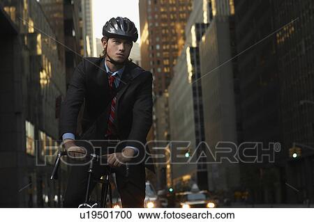 Stock Image - Man standing by bicycle in street, portrait. Fotosearch