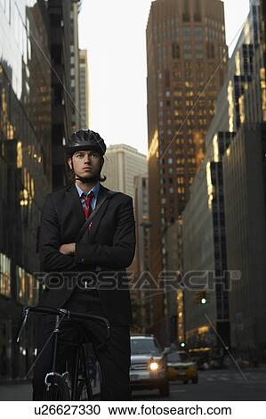 Stock Image - Man standing by bicycle in street, portrait. Fotosearch