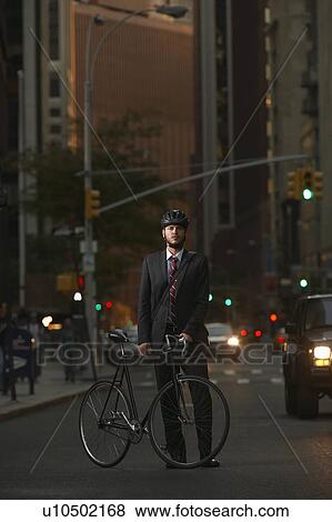 Stock Photo - Man standing by bicycle in street, portrait. Fotosearch