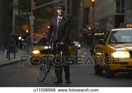 Stock Photo - Man standing by bicycle in street, portrait. Fotosearch