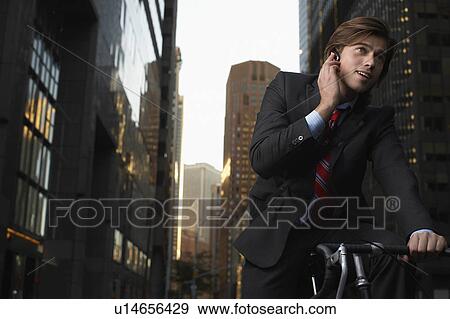 Man standing by bicycle in street, talking on mobile phone, low angle view View Large Photo Image Stock Photo - Man standing by bicycle in street, talking on mobile phone, low angle view. Fotosearch