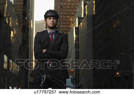 Stock Photo - Man standing by bicycle in street, portrait. Fotosearch