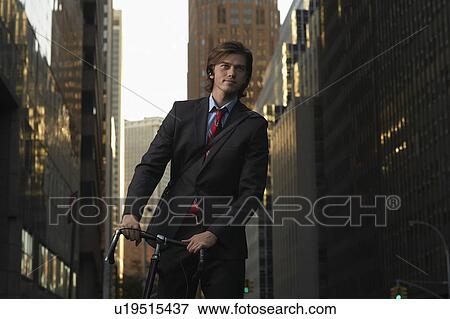 Stock Photo - Man standing by bicycle in street, portrait. Fotosearch