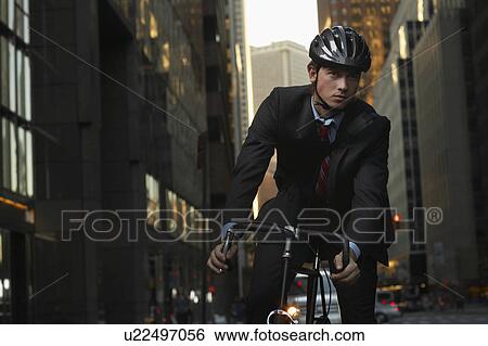 Stock Photograph - Man standing by bicycle in street, portrait. Fotosearch