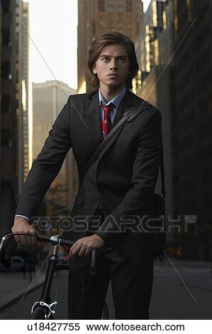 Stock Photography - Man standing by bicycle in street, portrait. Fotosearch