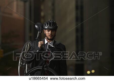 Picture - Man standing on street, carrying bicycle, portrait. Fotosearch
