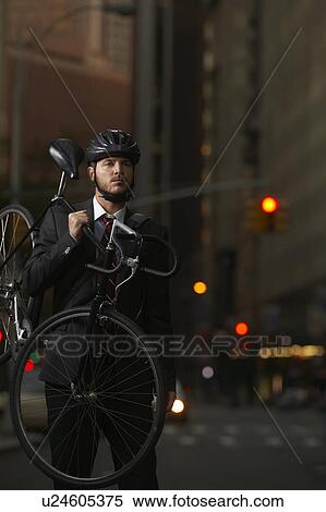 Stock Photography - Man standing on street, carrying bicycle, portrait. Fotosearch