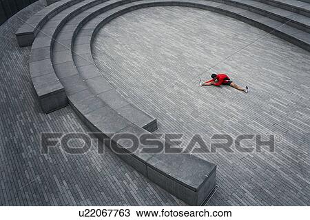Stock Image - Man stretching in the Scoop amphitheatre, London, England, elevated view. Fotosearch