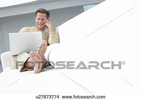 Picture - Man using laptop on sofa in living room. Fotosearch