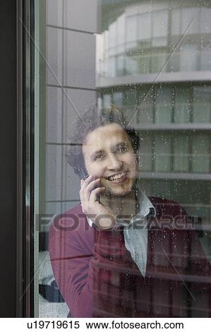 Man using mobile phone standing by window View Large Photo Image Stock Photography - Man using mobile phone standing by window. Fotosearch