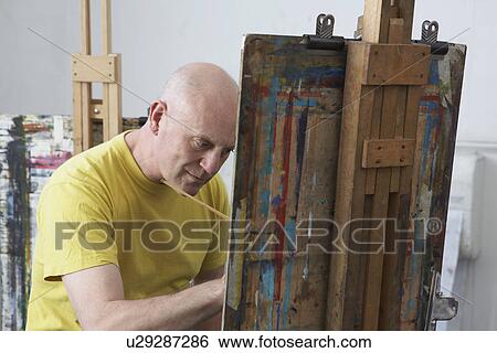 Stock Photograph - Mature male artist painting at easel. Fotosearch