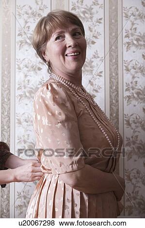Stock Photo - Mature woman waits while her dress is fastened. Fotosearch