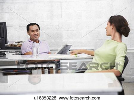 Mid adult man and woman sitting at desks, talking View Large Photo Image Stock Photo - Mid adult man and woman sitting at desks, talking. Fotosearch