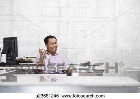 Mid adult man sitting at desk in office, gesturing View Large Photo Image Stock Photograph - Mid adult man sitting at desk in office, gesturing. Fotosearch
