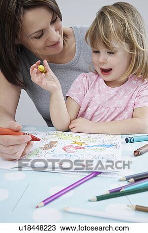 Stock Image - Mother and daughter (3-4) colouring in book. Fotosearch