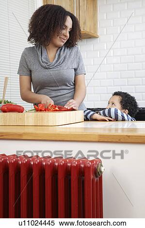 Stock Photography - Mother chopping pepper and looking at son (5-6). Fotosearch