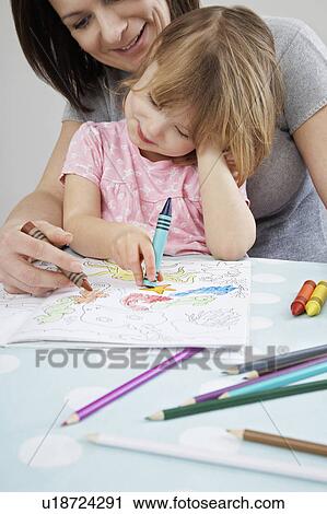 Stock Image - Mother helping daughter (3-4) with colouring in book. Fotosearch