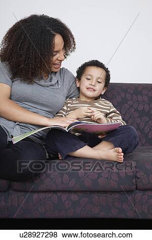 Stock Photo - Mother reading book with son (5-6) on sofa. Fotosearch