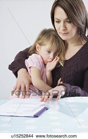 Mother with daughter (3-4) on laps looking at paperwork View Large Photo Image Picture - Mother with daughter (3-4) on laps looking at paperwork. Fotosearch