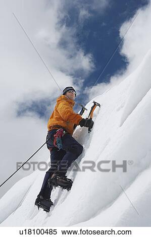 Stock Photography - Mountain climber going up snowy slope with axes. Fotosearch