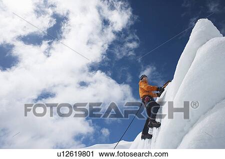 Stock Image - Mountain climber reaching snowy peak. Fotosearch