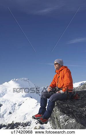 Mountain climber sitting on edge of mountain peak View Large Photo Image Stock Photo - Mountain climber sitting on edge of mountain peak. Fotosearch