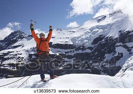 Stock Image - Mountain climber with arms raised on top of snowy peak. Fotosearch