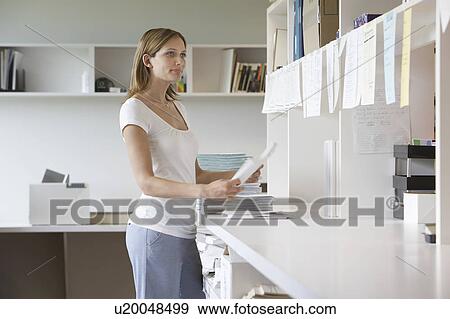 Stock Photo - Office worker holding paper notes standing in office, side view. Fotosearch