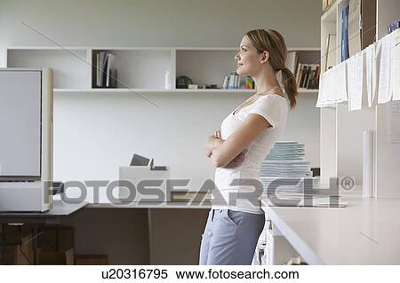 Stock Photography - Office worker leaning on bench in office, side view. Fotosearch