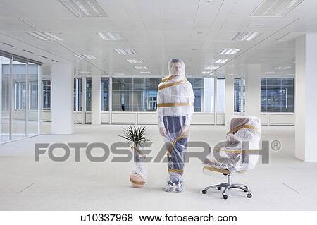 Stock Photo - Office worker, swivel chair and potted plant covered with bubble wrap and tape in empty office space. Fotosearch